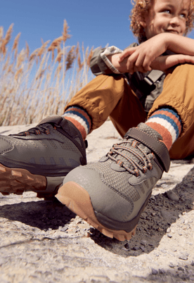 A child putting on brown Merrell shoes for an outdoor adventure.